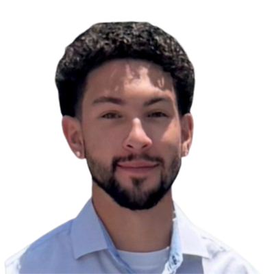 A young man with curly hair and a beard smiles slightly. He wears a light blue shirt on a white background